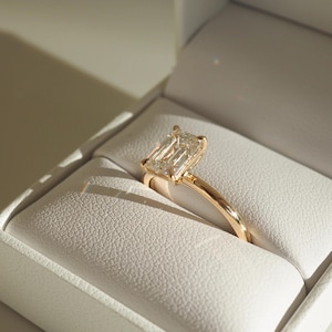 May include: A gold ring with a large, clear, emerald-cut diamond in a white box.
