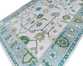 May include: A white rug with a blue and green geometric pattern. The rug has a light blue border with a white and green design.