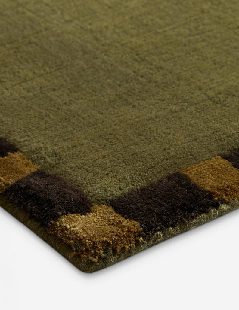 May include: Close-up of a green rug with a brown and tan checkered border. The rug has a textured surface and a soft, plush appearance. The color palette is earthy and natural.