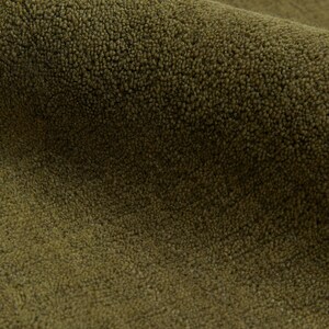 May include: Close-up of a section of olive green fabric with a textured, looped pile. The fabric is folded, revealing the depth and density of the material. The color is a muted, earthy tone, suggesting a natural fiber.