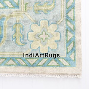 May include: A light blue and cream colored rug with a geometric pattern. The rug has a fringe border and the text "IndiArtRugs" is printed in the center.