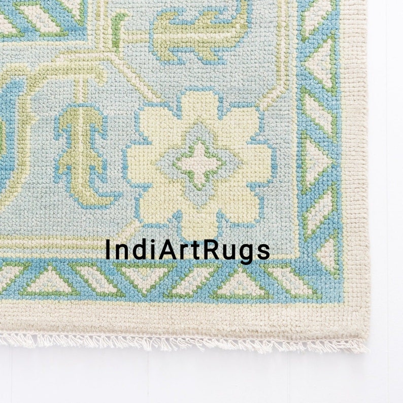 May include: A light blue and cream colored rug with a geometric pattern. The rug has a fringe border and the text "IndiArtRugs" is printed in the center.