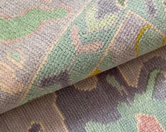May include: A close-up of a soft, pastel-colored rug with a geometric pattern. The rug is made of a fluffy, textured material and features shades of pink, blue, green, and white.