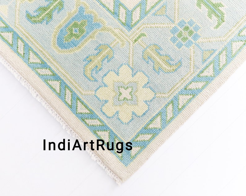 May include: Close-up of a corner of a light blue and green patterned rug with a white fringe. The rug has a geometric design with floral motifs.
