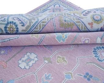 Könnte beinhalten: Aufgerollter Teppich mit einem aufwendigen Muster in Rosa, Blau und Creme. Das Design zeigt florale und geometrische Motive mit einem detaillierten Rand. Die Textur und Farbgebung des Teppichs deuten auf einen traditionellen oder Vintage-Stil hin.