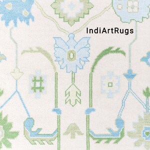 May include: A white rug with a repeating pattern of green and blue floral designs. The text "IndiArtRugs" is in the center of the rug.