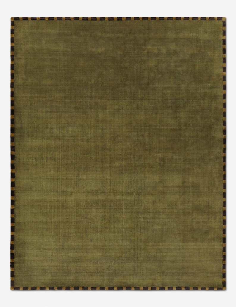 May include: A rectangular olive green rug with a textured surface. The rug has a border of alternating dark brown and tan rectangles. The rug is a solid color with a subtle woven pattern.