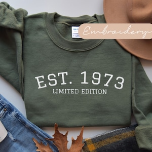 May include: A green sweatshirt with white embroidered text that reads "EST. 1973 LIMITED EDITION".