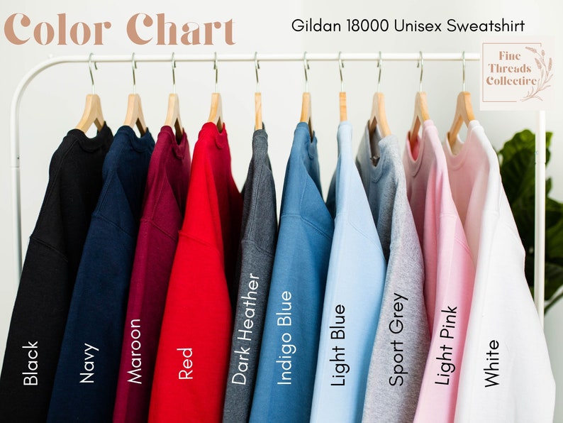 May include: A color chart displays Gildan 18000 unisex sweatshirts in various colors. The sweatshirts are hanging on a white rack. Colors include black, navy, maroon, red, dark heather, indigo blue, light blue, sport grey, light pink, and white.