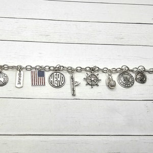 May include: A silver charm bracelet with various charms, including a globe, a flag, a ship's wheel, a grenade, and a tag that says "BRAVE".
