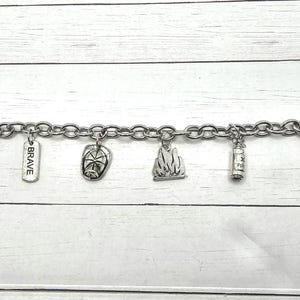 Op de afbeelding: Een zilveren armband met meerdere bedels, waaronder een brandweerhelm, een brandblusser, een vlam en een bedel met de tekst "Mijn hart behoort aan een brandweerman".