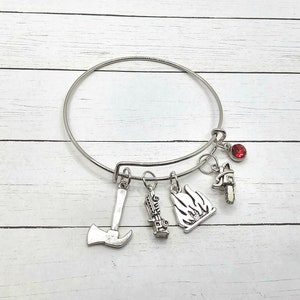 May include: A silver bangle bracelet with five charms: an axe, a fire hydrant, a flame, a chainsaw, and a red rhinestone.