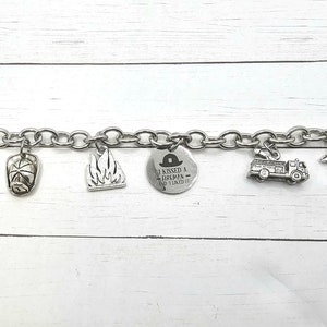 Può includere: Un braccialetto con ciondoli in argento con vari ciondoli a tema pompiere, tra cui un idrante, un cappello da pompiere, un camion dei pompieri, un dalmata e un ciondolo con il testo "Ho baciato un pompiere - e mi è piaciuto".