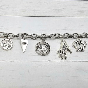 May include: A silver charm bracelet with a variety of charms, including a lotus flower, a bull, a heart with an eye, a hand with an eye, an elephant, a zodiac sign, and an evil eye charm.