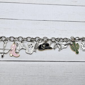 May include: A silver charm bracelet with a variety of western-themed charms, including a cowboy hat, a cactus, a horseshoe, a boot, and a skull.
