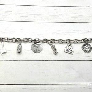 Op de afbeelding: Een zilveren armband met brandweercharms. De charms omvatten een brandkraan, een bijl, een brandweerwagen, een vuur en een brandweerbadge. De armband heeft ook een charm met de tekst "Mijn hart behoort aan een brandweerman".