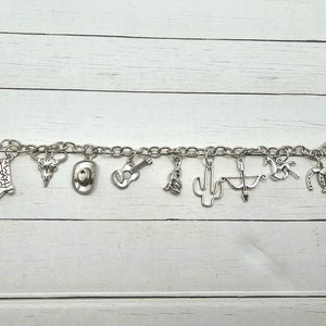 May include: A silver charm bracelet with various western-themed charms, including a cowboy boot, a skull, a cowboy hat, a guitar, a cactus, a horseshoe, and a horse.