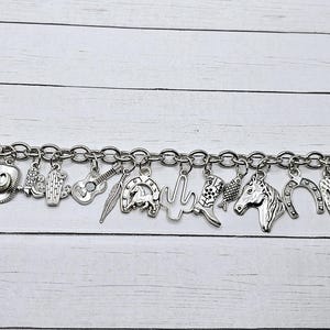 May include: A silver charm bracelet with a variety of western-themed charms, including horseshoes, cowboy hats, cacti, and boots.