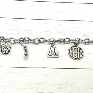 Può includere: Un braccialetto con ciondoli in argento con diversi ciondoli, tra cui un estintore, un casco da pompiere, un'ascia, una fiamma e un cerchio con la parola "HERO" su di esso.