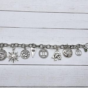 May include: A silver charm bracelet with various zodiac signs, including Gemini, Pisces, and the sun. The bracelet also features a heart charm with an eye design and a crescent moon charm.