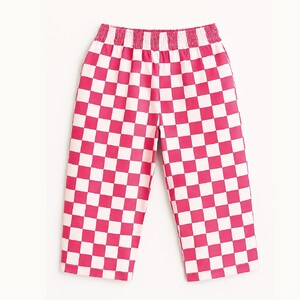 May include: Pink and white checkered pants with an elastic waistband. The cropped pants feature a bold checkerboard pattern in a vibrant pink and white color scheme. The pants are made of a lightweight material.