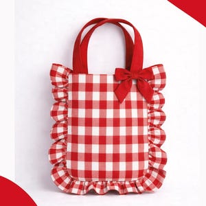 Puede incluir: Bolso tote a cuadros rojos y blancos con bordes con volantes y un lazo rojo. El bolso tiene asas rojas y el texto "Lucy Rise Kids Wear". Diseñado para niños.