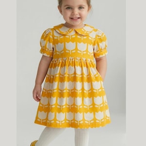 May include: A yellow dress with a white tulip pattern, a matching bow, and yellow shoes. The dress has a Peter Pan collar and short sleeves. The child is also wearing white tights. The dress is a cheerful outfit for a young girl.