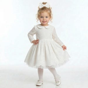 May include: A white eyelet dress with a Peter Pan collar and long sleeves. The dress features a full skirt and is paired with white tights and shoes. A white bow adorns the hair.