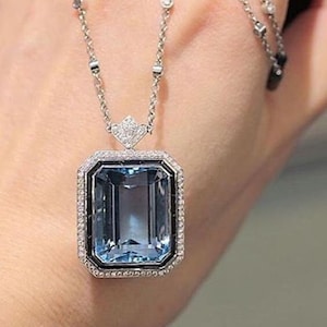 Puede incluir: Un collar de plata con un gran colgante rectangular de piedra azul. El colgante está rodeado por un borde de diamantes más pequeños y ónix negro. El collar está hecho de una cadena delicada con detalles alternos de ónix negro y diamantes.