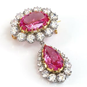 Op de afbeelding: Een roze edelsteen hanger met een peervormige druppel en een ronde, bezel-gezet steen. De hanger is omgeven door een halo van kleinere, ronde, heldere edelstenen.