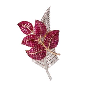 Op de afbeelding: Een broche van robijnen en diamanten in de vorm van een blad. De bladeren zijn bezet met rode robijnen en de steel is bezet met diamanten.