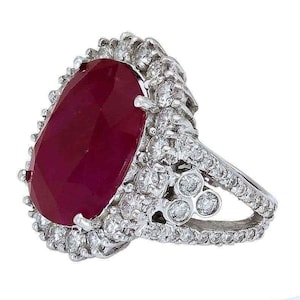 May include: A striking ring featuring a large, oval-cut ruby. The ruby is a rich, deep red, encircled by a halo of small, clear diamonds. The ring's band is also set with diamonds, adding to its brilliance.