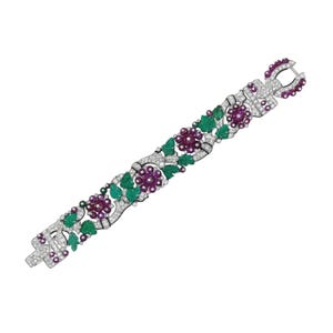 Può includere: Un bracciale ornato con un design floreale, con grappoli alternati di pietre preziose viola e verdi, accentuati da pietre chiare e scintillanti. Il bracciale ha una chiusura a fermaglio ed è posto su uno sfondo bianco.