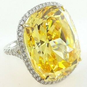 May include: A large, eye-catching ring featuring a vibrant yellow gemstone. The gemstone is rectangular with a faceted cut, surrounded by a halo of smaller, clear stones. The band is silver-toned, adding to the ring's elegant design.