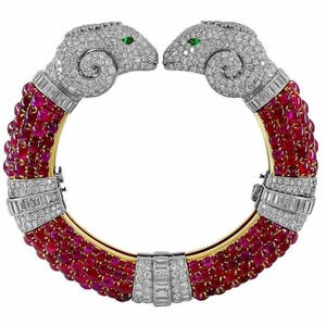 Puede incluir: Un brazalete de oro con dos detalles de cabeza de carnero engastados con diamantes y esmeraldas. El brazalete está adornado con filas de cuentas de rubí.