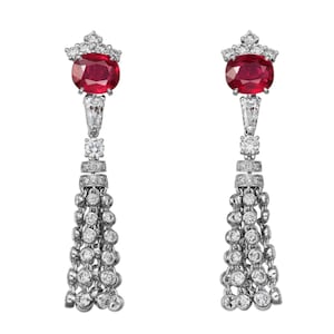 Puede incluir: Un par de pendientes colgantes. Cada pendiente presenta un gran rubí ovalado en la parte superior, engastado con diamantes más pequeños en un diseño similar a una corona. Debajo del rubí, una serie de diamantes y una borla de diamantes redondos completan el diseño.