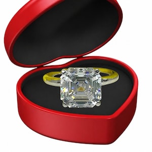 Puede incluir: Un anillo de diamantes con una piedra grande de talla cuadrada se muestra en una caja roja en forma de corazón abierta. El anillo tiene una banda dorada. El interior de la caja es negro.