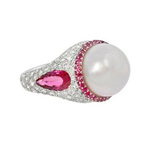 May include: A silver ring with a large white pearl surrounded by pink gemstones. Two smaller pink gemstones are set on either side of the pearl.