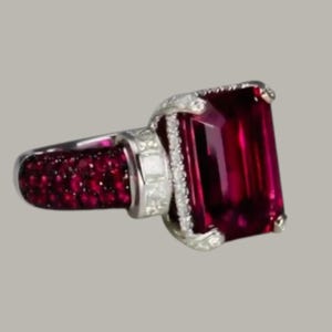 May include: A silver ring with a large, rectangular, deep red gemstone. The ring's band is set with smaller, round red gemstones, and the setting is embellished with clear, sparkling accent stones.
