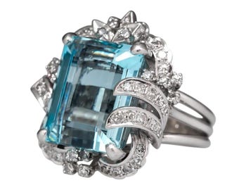 May include: A silver ring with a large, light blue aquamarine gemstone surrounded by smaller diamonds. The ring has a delicate, floral design.