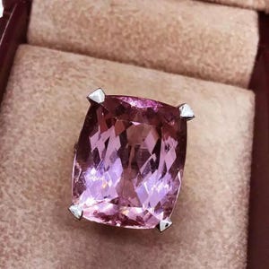 May include: A pink gemstone ring with a cushion-cut stone set in a silver setting.