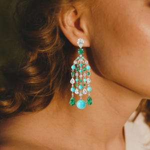 May include: A pair of long, dangling earrings with a cascade of turquoise and emerald green gemstones. The earrings are set in gold and feature a large, round turquoise stone at the bottom.