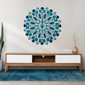 Può includere: Un orologio da parete decorativo con un design geometrico a strati nei toni del verde acqua, blu navy e bianco. Il quadrante presenta numeri arabi e una lancetta centrale. L'orologio è montato su una parete bianca sopra un mobile in legno.