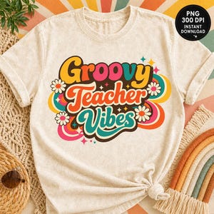 May include: Cream-colored t-shirt with the words "Groovy Teacher Vibes" in a colorful, retro design. The design includes daisies, swirls, and stars. The shirt is knotted at the bottom.