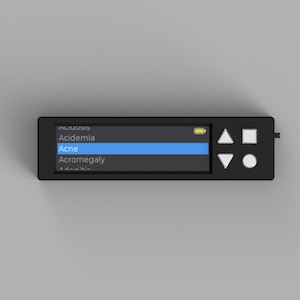 Puede incluir: Un dispositivo electrónico negro con una pantalla que muestra términos médicos, incluyendo "Acne". La pantalla resalta la palabra "Acne" en azul. El dispositivo tiene varios botones y un pequeño indicador de energía.