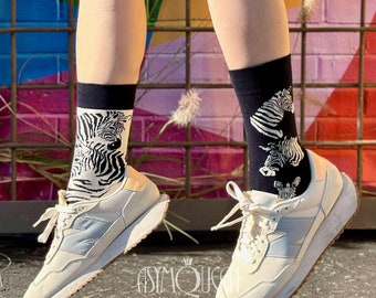 May include: A person wearing white sneakers with black and white zebra print socks. The sneakers have a light blue accent on the side.