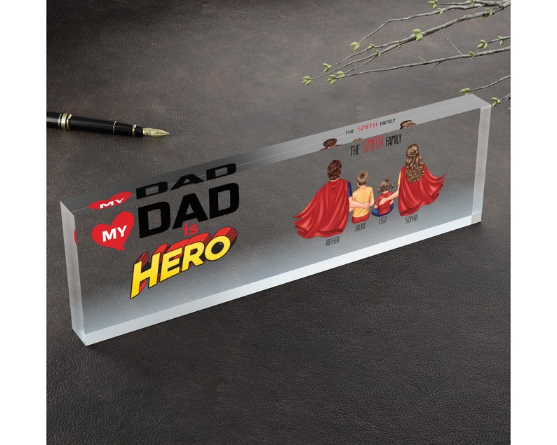 K&ouml;nnte beinhalten: Ein transparenter Acrylblock mit dem Text "My Dad is Hero" in einer Comic-Schriftart. Der Block zeigt auch eine f&uuml;nfk&ouml;pfige Familie, die rote Superhelden-Umh&auml;nge tr&auml;gt, mit ihren Namen darunter.