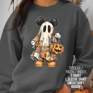 May include: Dark gray sweatshirt featuring a cartoon ghost character with Mickey Mouse ears, holding a jack-o'-lantern. The ghost is draped in a patchwork quilt. Text on the image reads: "TODDLER / YOUTH / UNISEX T-SHIRT L.SLEEVE SHIRT SWEATSHIRT HOODIE."