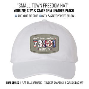 May include: White baseball cap with a leather patch that reads "Small Town Freedom" and displays the zip code 73001 and "Austin, TX". The patch has red, white, and blue accents. The hat is available in three styles.