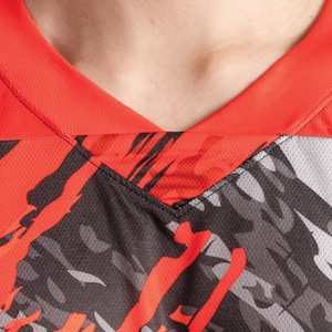 May include: Close-up of a red and black athletic jersey with a v-neck collar. The jersey has a camouflage pattern with red and black accents.